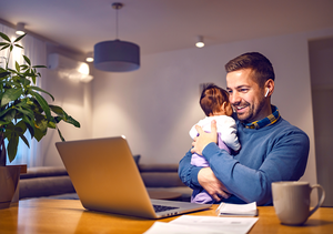 Ein Vater sitzt mit einem Baby vor dem Laptop und