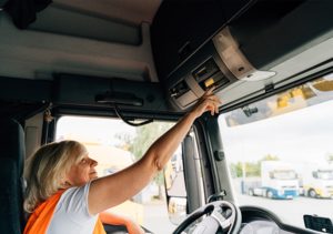 Eine Fahrerin sitzt in einem LKW und bedient den Fahrtenschreiber