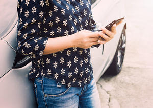 Frau, die ein Handy benutzt und sich an ein Auto anlehnt